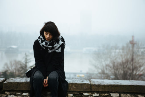 Girl sitting alone in the cold. Fog in the background.