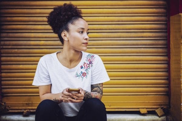 Woman with phone in hand looking away, reflecting struggles of drunkorexia.