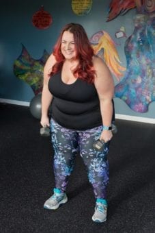 woman in leggings and a black top smilier and holding hand weights