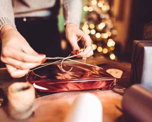 Woman wrapping holiday gift with a ribbon.