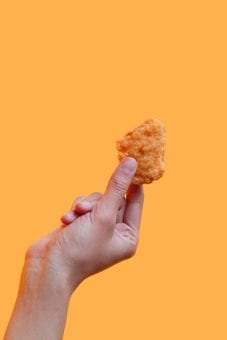 person holding a chicken nugget on an orange background
