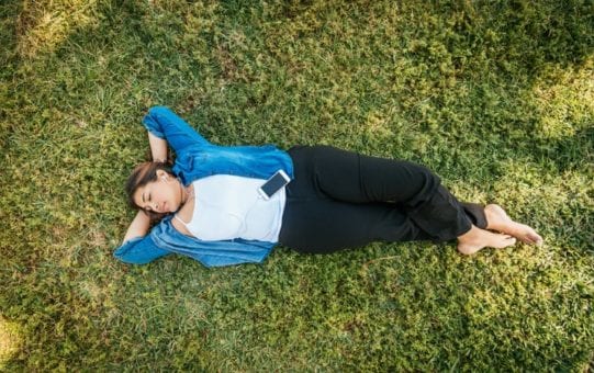 Woman laying on the grass listening to music on her phone.