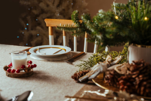 Decorated holiday dinner table with pine branch, candle, pinecones and plate setting.