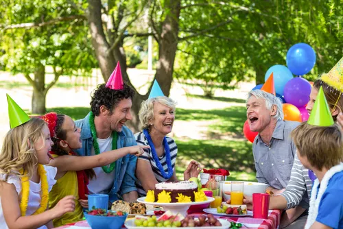 Family celebrating a birthday party outdoors at a picnic table.
